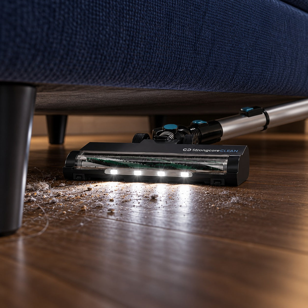 CLEAN's four white LEDs revealing dry dust beneath a navy sofa, with the floor head inside the sofa's footprint.